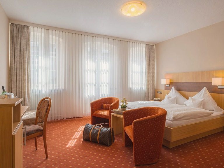 Doppelzimmer „Braumeister“ mit Doppelbett, Sesseln und großem Fenster.