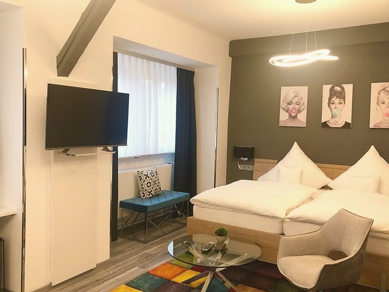 Comfort-Zimmer mit Doppelbett, Sessel und Flachbildfernseher.