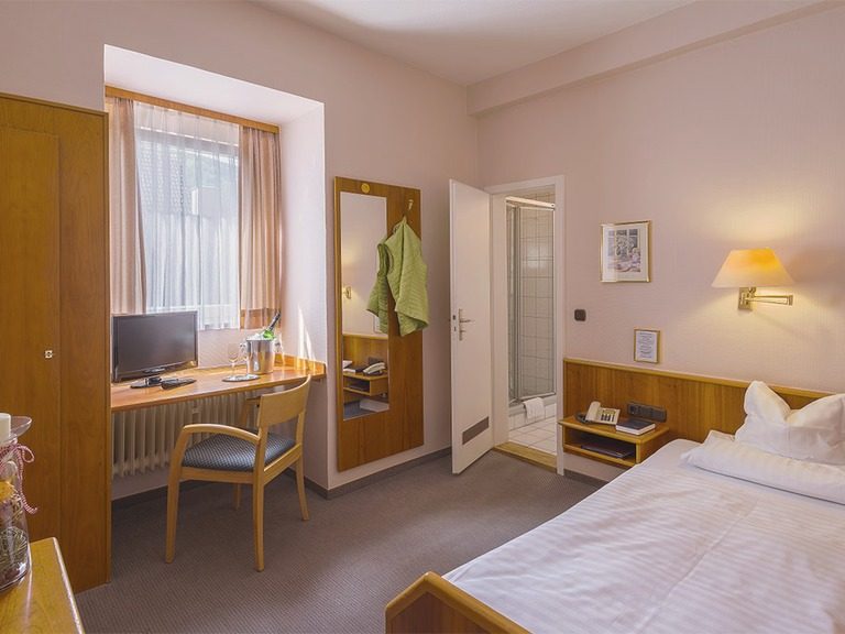Einzelzimmer mit Bett, Schreibtisch und Kleiderschrank.