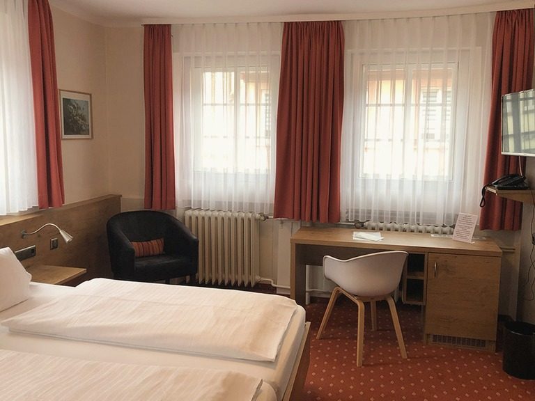 Doppelzimmer „Mälzer“ mit Bett, Schreibtisch und Sessel am Fenster.